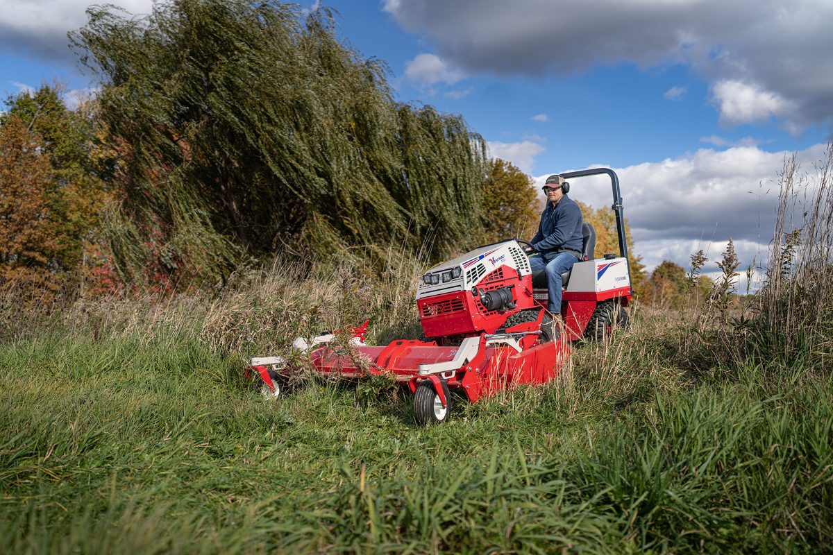 Ventrac with a rough-cut deck working through long grass beside a tree line
